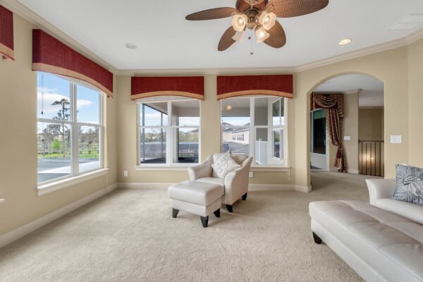 Spacious living room with large windows, elegant ceiling fan, and plush carpet, showcasing views of the lake in a luxury home at 1837 Lake Roberts Landing Dr, Winter Garden, FL.