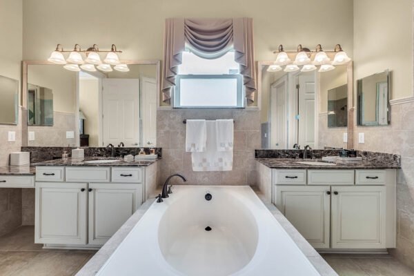 Master bathroom featuring dual vanities with granite countertops, large soaking tub, and elegant lighting, showcasing luxury design elements in a lakefront property at 1837 Lake Roberts Landing Dr, Winter Garden, FL.
