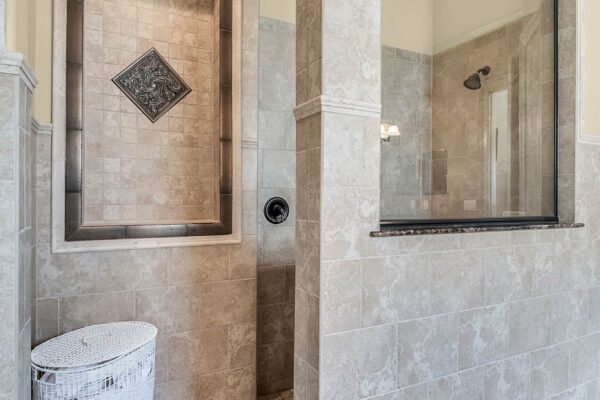 Luxurious master bathroom featuring a spacious walk-in shower, elegant tile work, and a decorative accent tile, with a stylish laundry basket in the corner.