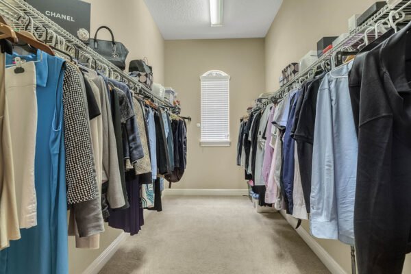 Walk-in closet featuring organized clothing on hangers, designer bags, and ample natural light from a window, showcasing luxury home storage in a lakefront property at 1837 Lake Roberts Landing Dr, Winter Garden, FL.