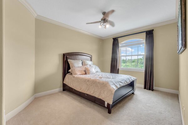 Spacious bedroom with a queen-sized bed, plush bedding, and large window showcasing scenic views, featuring crown molding and soft carpet, ideal for the luxury home at 1837 Lake Roberts Landing Dr, Winter Garden, FL.
