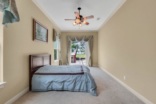 Spacious bedroom with a king-sized bed, elegant ceiling fan, and large windows offering views of the outdoor pool area in a luxury lakefront home at 1837 Lake Roberts Landing Dr, Winter Garden, FL.