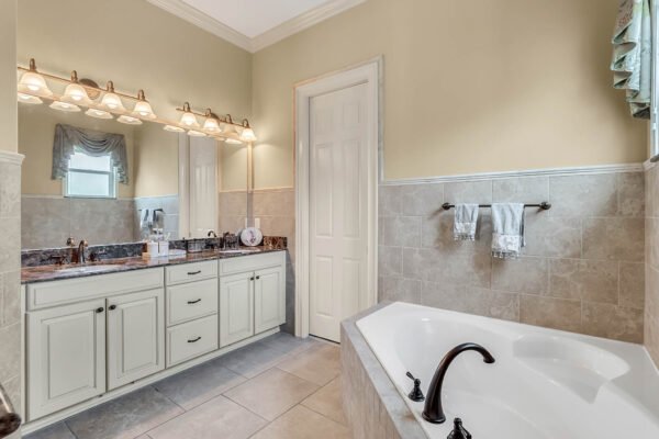 Spacious bathroom featuring double vanity with granite countertops, large soaking tub, and elegant lighting, showcasing luxury amenities in a lakefront property at 1837 Lake Roberts Landing Dr, Winter Garden, FL.