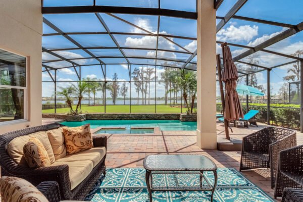 Lakefront view from a screened lanai featuring a swimming pool, outdoor seating with decorative cushions, and a patio area with a tranquil atmosphere at 1837 Lake Roberts Landing Dr, Winter Garden, FL.