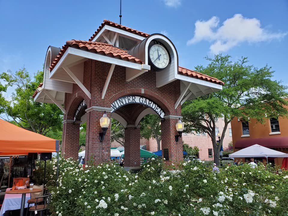 Winter Garden archway with clock, surrounded by flowers and market tents, representing local charm in Winter Garden real estate insights.