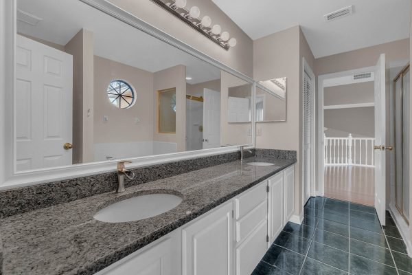 Spacious bathroom featuring dual sinks with granite countertops, large mirror, and natural light from circular window, showcasing modern design in Orlando home for sale at 12847 Sharp Shined Street.