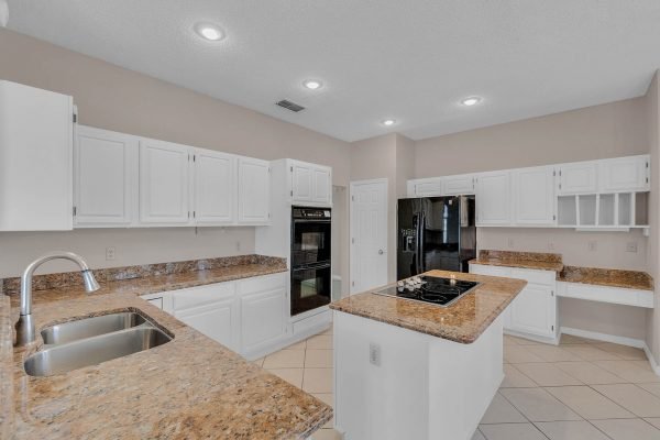 Modern kitchen with granite countertops, white cabinetry, stainless steel appliances, and tile flooring, showcasing a spacious layout ideal for family gatherings in the home at 12847 Sharp Shined Street, Orlando, FL.