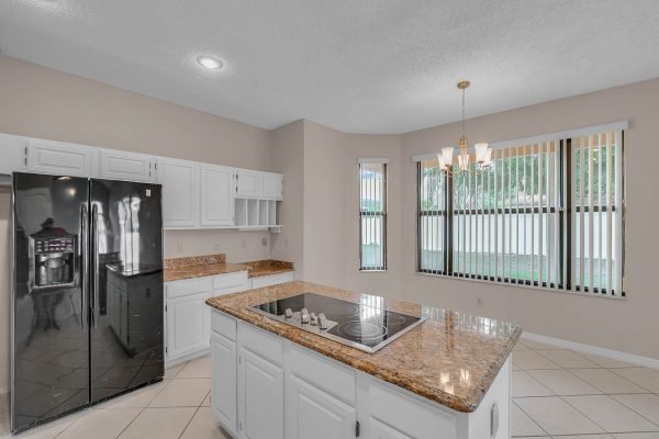 Modern kitchen with granite countertops, black refrigerator, white cabinetry, and natural light from large windows, showcasing the inviting space of the home at 12847 Sharp Shined Street, Orlando, FL.
