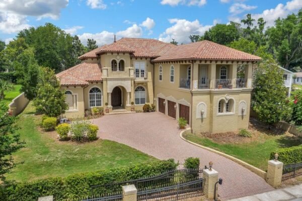 Mediterranean-style estate at 517 East 6th Avenue in Windermere, FL, featuring a spacious driveway, lush landscaping, and a tile roof, highlighting luxury living with no HOA.