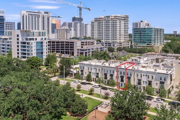 Aerial view of 647 E Jackson St, Orlando, showcasing the Brownstones of Thornton Park, surrounded by modern buildings and greenery, emphasizing urban living and proximity to downtown amenities.