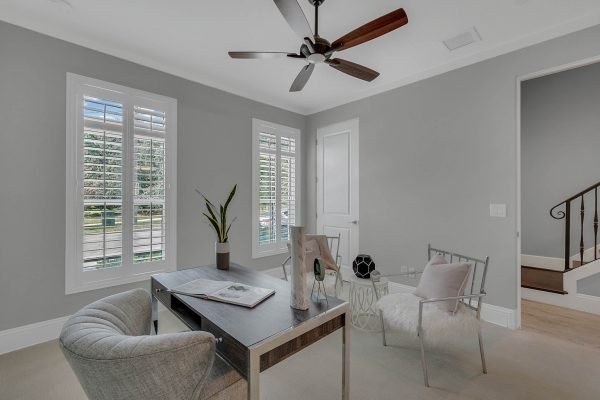 Modern home office with gray walls, stylish furnishings, large windows with shutters, and a ceiling fan, ideal for remote work near downtown Orlando.