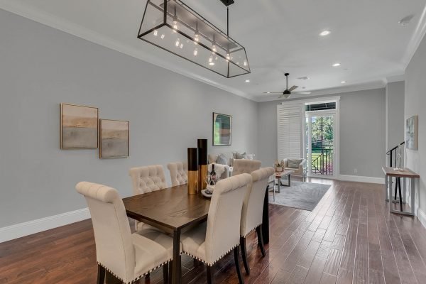 Modern dining area featuring a wooden table with upholstered chairs, elegant lighting fixture, and artwork on grey walls, showcasing a spacious layout with natural light from large windows and access to a patio, ideal for upscale living in downtown Orlando.