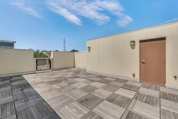Private rooftop deck with wooden tile flooring, featuring a door leading to the interior, and a clear blue sky in the background, ideal for entertaining or relaxing in downtown Orlando.