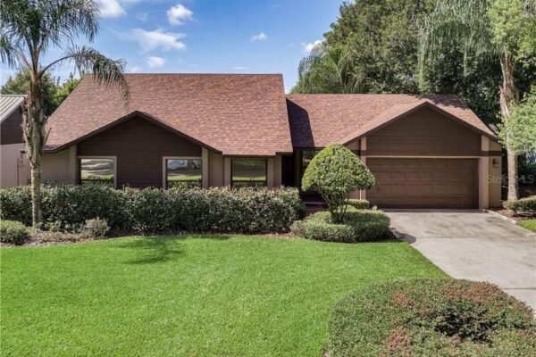 Single-story home with a brown exterior, manicured lawn, and palm trees, showcasing a welcoming front entrance and a two-car garage, relevant to affordable real estate listings in Windermere, FL.