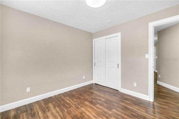 Interior view of a remodeled room featuring light brown walls, a wooden floor, and double white doors leading to a closet, relevant to the affordable pool home listing in Orlando, FL.
