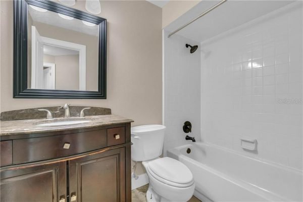 Bathroom with dark wood vanity, granite countertop, mirror, and white bathtub in a remodeled home, reflecting features relevant to affordable real estate listings in Windermere, Florida.