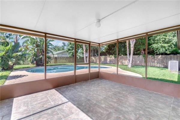Screened patio overlooking a private pool and spacious fenced yard, featuring tropical plants and a well-maintained lawn, ideal for outdoor living in Florida.