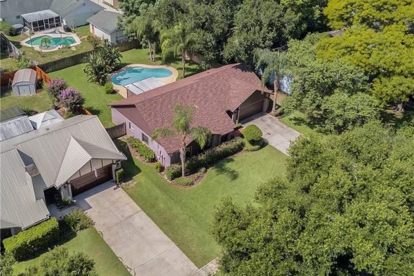 Aerial view of a single-family home in Orlando, FL, featuring a large fenced yard, palm trees, and a nearby swimming pool, highlighting the outdoor space ideal for family living.