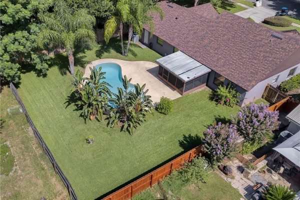 Aerial view of a backyard featuring a swimming pool, lush greenery, palm trees, and a fenced yard, showcasing an inviting outdoor space ideal for family enjoyment in Windermere, Florida.