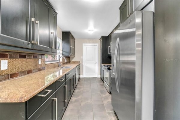 Modern kitchen with dark cabinetry, granite countertops, stainless steel appliances, and tiled flooring, showcasing a remodeled interior relevant to affordable homes in Windermere, Orlando.
