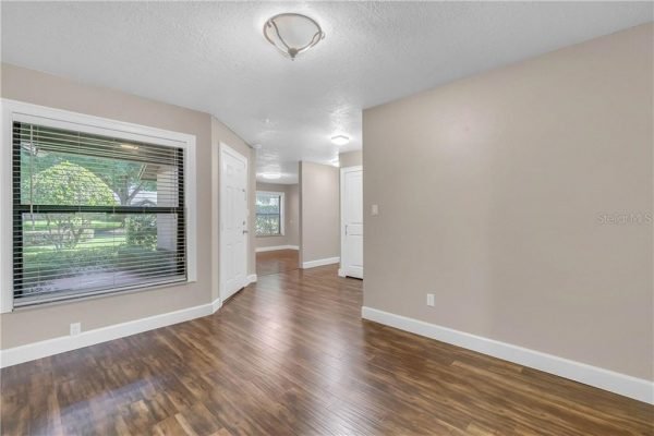 Interior view of a freshly painted living space with hardwood flooring, featuring large windows allowing natural light, and doors leading to other rooms, highlighting the home's updated condition in Orlando, FL.
