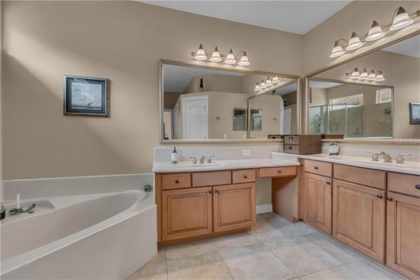 Spacious master bathroom featuring dual sinks, wooden cabinetry, large mirrors, and a soaking tub, emphasizing luxury and comfort in the Winter Garden home at 12703 Dallington Terrace.