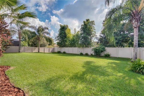 Spacious fenced backyard with lush green lawn, palm trees, and privacy hedges at 12703 Dallington Terrace, Winter Garden, FL.