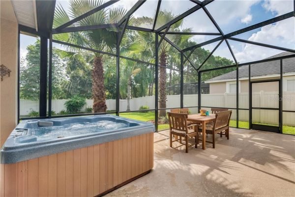 Hot tub and outdoor dining area in screened lanai surrounded by palm trees and fenced yard at 12703 Dallington Terrace, Winter Garden, FL.