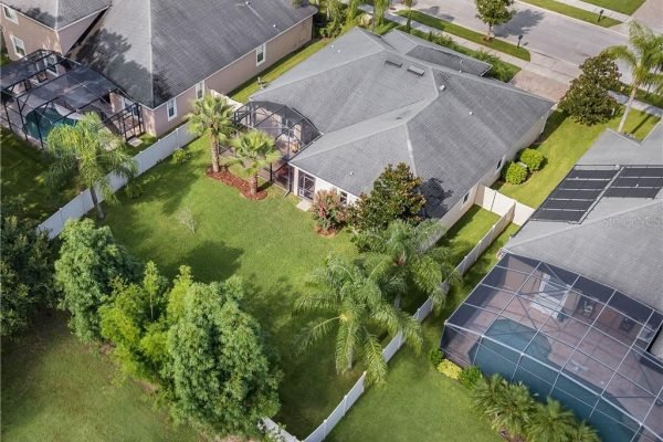 Aerial view of 12703 Dallington Terrace in Winter Garden, FL, showcasing a spacious fenced yard, palm trees, and neighboring homes, highlighting the property's outdoor space and privacy.