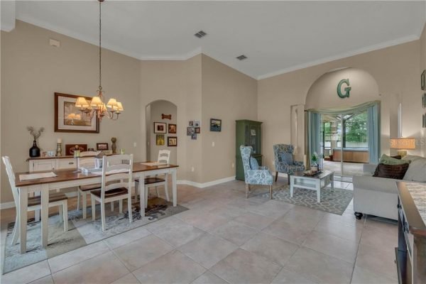 Dining area and living space of a Winter Garden home featuring a wooden dining table with white chairs, decorative lighting, and a cozy seating area with blue chairs, leading to a screened lanai, showcasing a bright and inviting atmosphere.