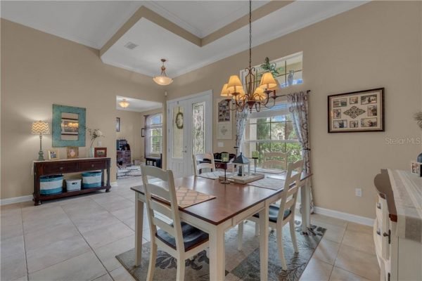 Dining area with a wooden table and chairs, featuring a chandelier, large windows providing natural light, and decorative elements, showcasing the inviting interior of the property at 12703 Dallington Terrace, Winter Garden, FL.