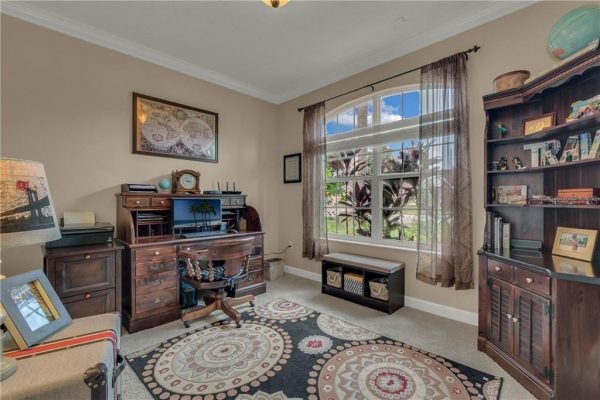 Home office with desk and computer, decorative bookshelf, large windows providing natural light, and patterned area rug, highlighting the spacious interior of the property at 12703 Dallington Terrace, Winter Garden, FL.