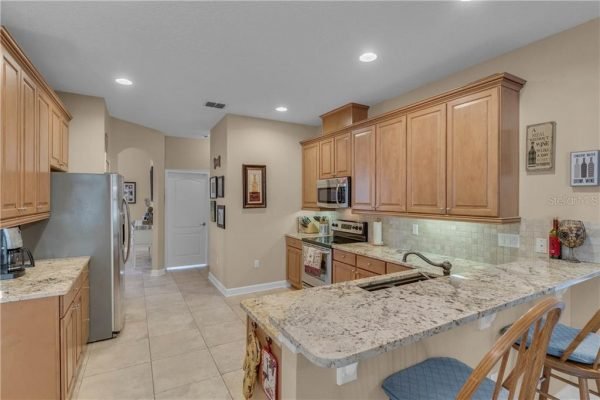 Kitchen interior featuring wood cabinetry, granite countertops, stainless steel appliances, and a breakfast bar with blue chairs, showcasing a spacious layout ideal for family living in a Winter Garden home.