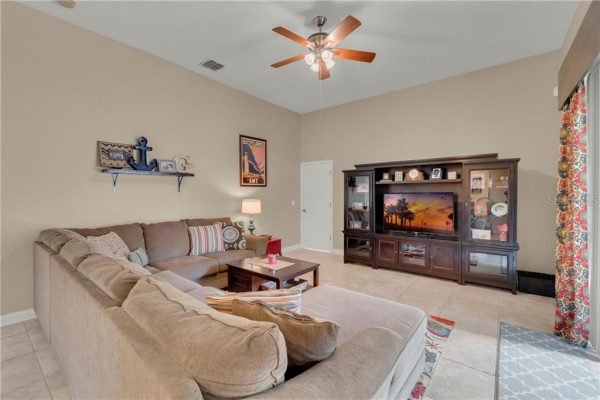 Cozy living room featuring a large sectional sofa, decorative throw pillows, and a wooden coffee table, with a TV unit displaying a scenic image, illuminated by natural light from a nearby window with patterned curtains.