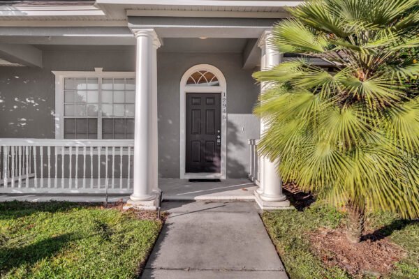 Front entrance of 12945 Overstreet Rd, Windermere, FL, featuring a dark door framed by white columns and a palm tree, highlighting the home's inviting curb appeal in the sought-after Windermere community.