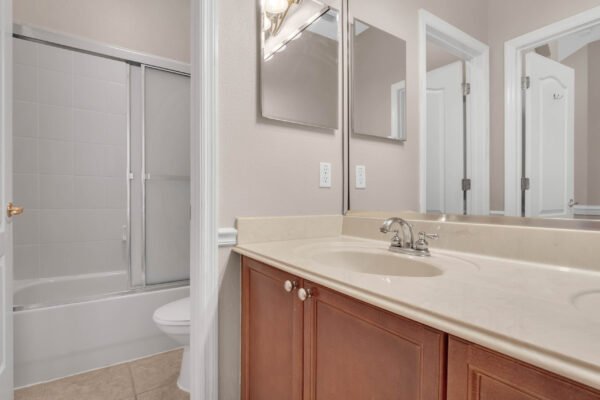 Bathroom interior featuring a double vanity with wooden cabinetry, mirrors, and a bathtub with sliding glass door, in a Windermere home for sale.