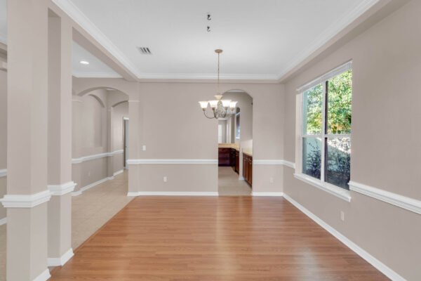 Spacious interior of a Windermere home featuring wood flooring, decorative crown molding, and a chandelier, with views into the kitchen and natural light from large windows.