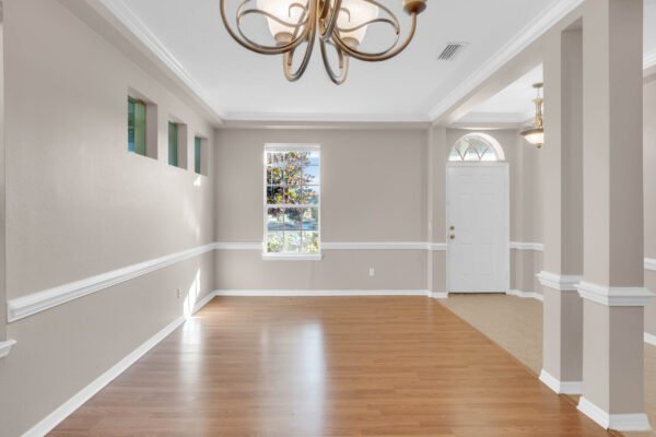 Spacious interior of a Windermere home featuring wood flooring, decorative chandelier, and natural light from windows, showcasing entryway and adjacent door to outside.