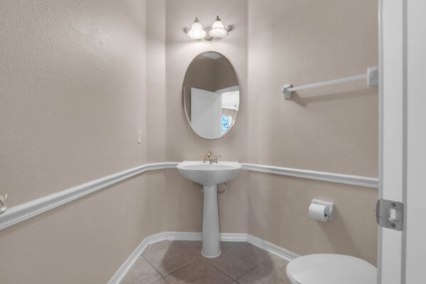 Powder room featuring a pedestal sink with a round mirror, light fixtures above, and neutral wall color, part of a 4-bedroom home in Windermere, FL.