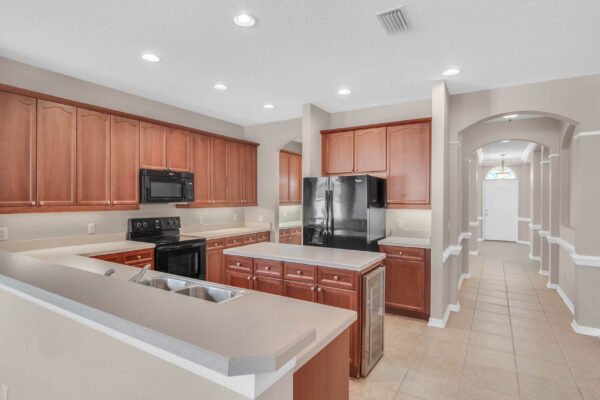 Modern kitchen with wood cabinets, black appliances, and open layout, featuring an island and adjoining hallway in a Windermere home for sale.