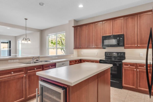 Modern kitchen with dark wood cabinetry, black appliances, and a central island featuring a wine cooler, showcasing a spacious layout and natural light from nearby windows, relevant to the Windermere real estate market.