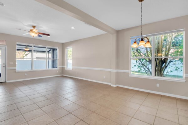 Spacious, carpet-free living area with tile flooring, ceiling fan, and large windows, showcasing natural light and views of the fenced yard in a Windermere home for sale.