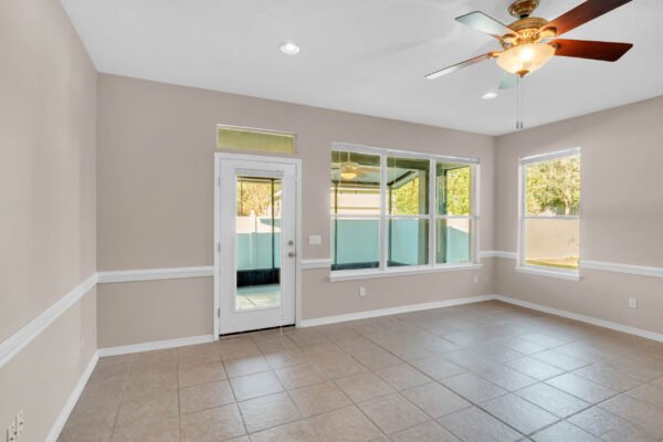 Spacious interior of a Windermere home featuring tile flooring, ceiling fan, and large windows, with a door leading to a fenced outdoor area.