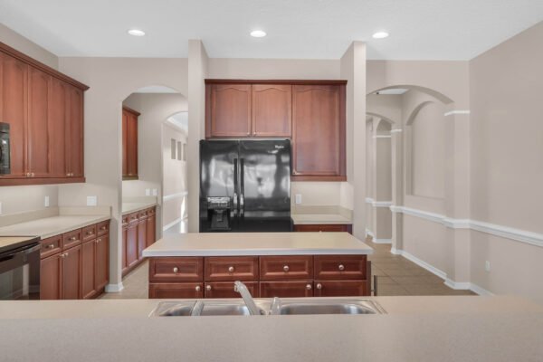 Modern kitchen with dark wood cabinetry, black refrigerator, and countertop overlooking open layout, showcasing functional design ideal for family living in Windermere, FL.