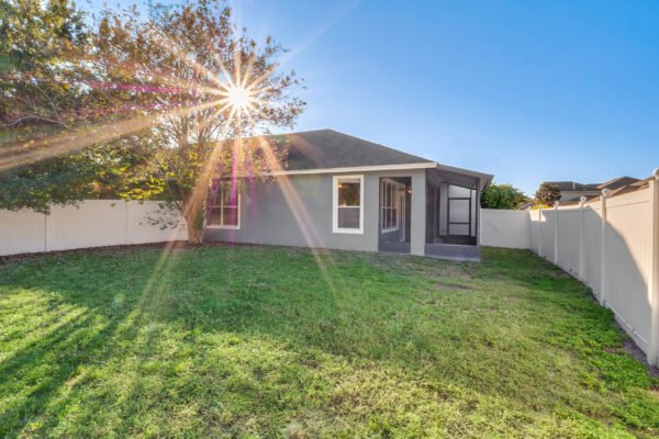 Backyard view of 12945 Overstreet Rd in Windermere, FL, showcasing a fenced lot, grassy area, and sun shining through a tree, highlighting the home's exterior design.