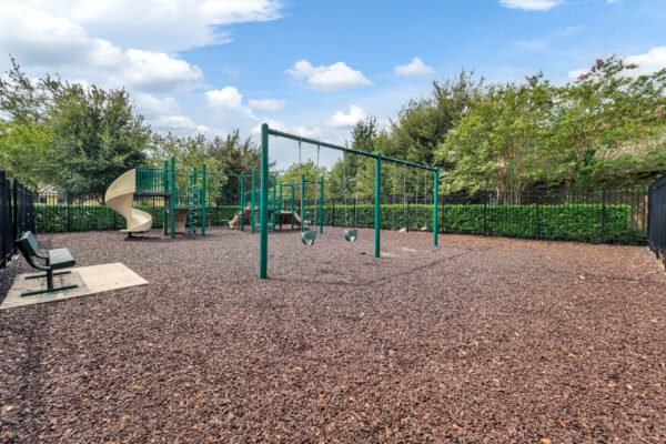 Playground area with swings, slide, and benches in a fenced setting surrounded by greenery, highlighting family-friendly features of the Windermere community.