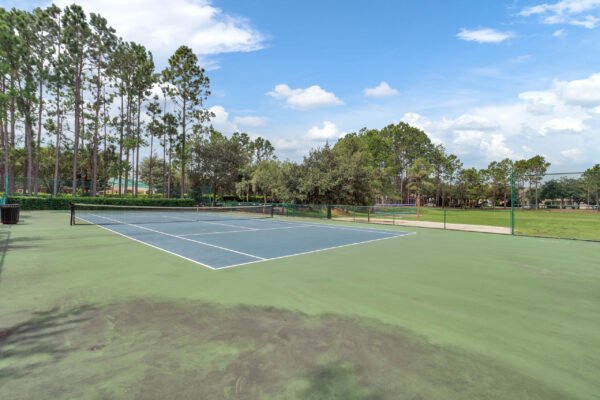 Tennis court in Windermere community surrounded by tall pine trees and green grass, showcasing recreational amenities close to residential listings.