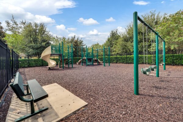 Playground equipment featuring a slide, climbing structure, and swings in a fenced area surrounded by trees, located in the Windermere community, ideal for families.