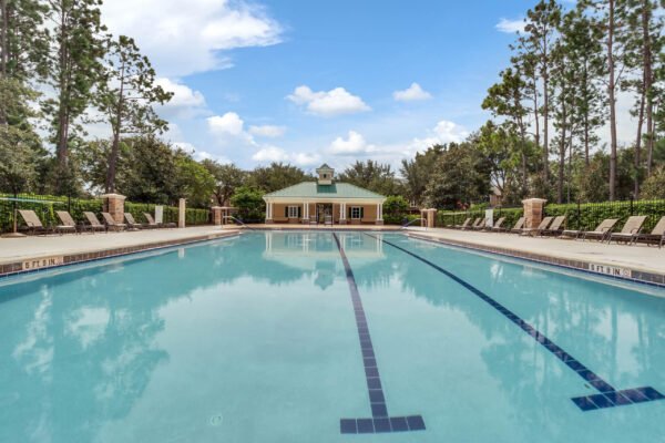 Community swimming pool in Windermere, Florida, featuring lounge chairs, a clubhouse in the background, and surrounded by lush greenery under a blue sky.