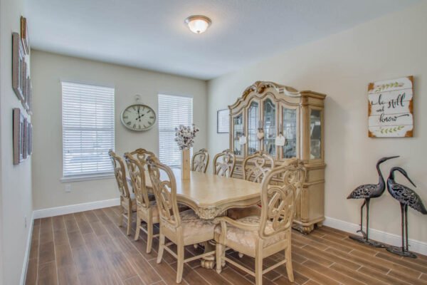 Dining room featuring a large wooden table with ornate chairs, a china cabinet, decorative wall art, and natural light from windows, highlighting a welcoming atmosphere in a modern home.